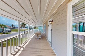 A covered porch with a wooden deck, white railings, and a view of the street and buildings in the background.