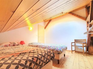 A bedroom with two beds, a wooden ceiling, a door, and a chair.