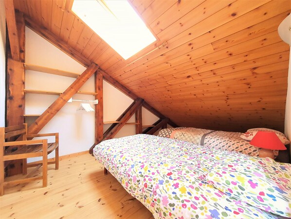 Habitación con techo inclinado, vigas de madera, cama con ropa de cama estampada, una silla y una pequeña mesa.