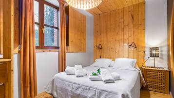 Un dormitorio con paneles de madera, una cama, sábanas blancas, una lámpara colgante y una mesita de noche con lámpara.