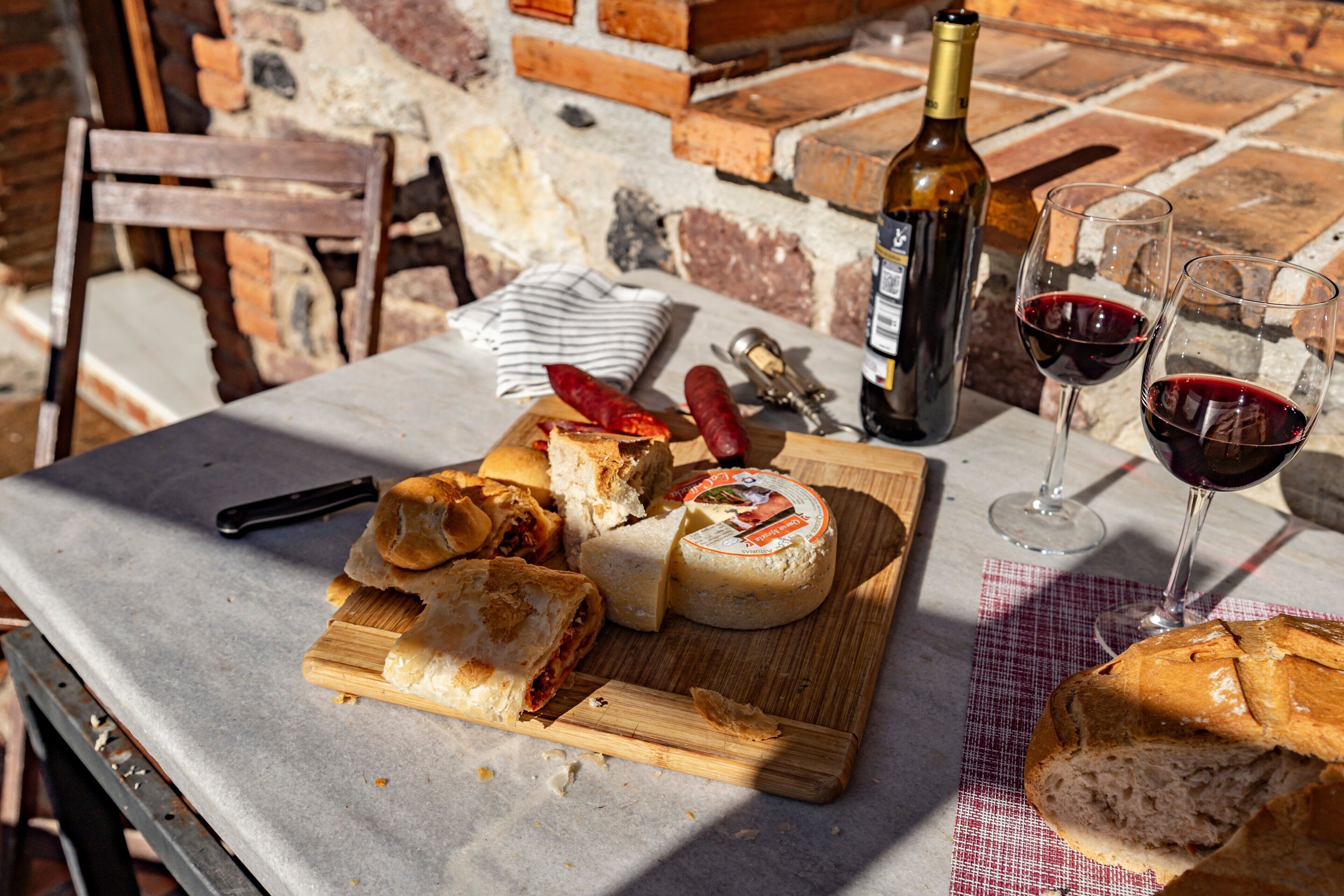 Et bord med en osteanretning, brød, en flaske vin og vinglas.