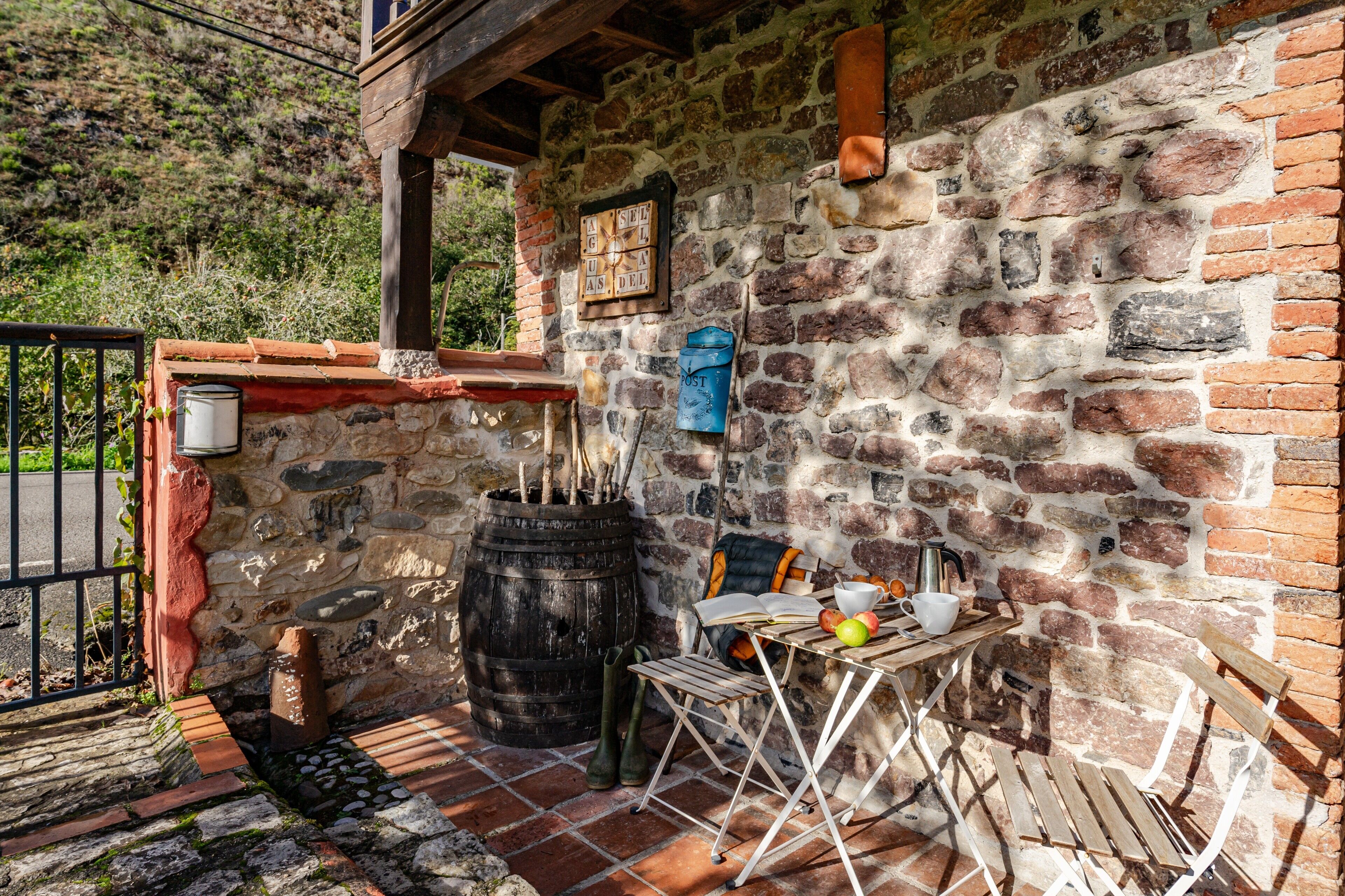A rustic stone wall with a wooden barrel, a table with a book, and a chair.