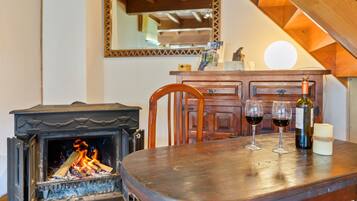 Una mesa de madera para comer con dos copas de vino y una vela, una chimenea, una silla de madera y un espejo en la pared.
