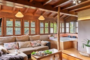 Um quarto acolhedor com sofá, mesa com bandeja de comida, banheira e janelas amplas com vista para o verde.
