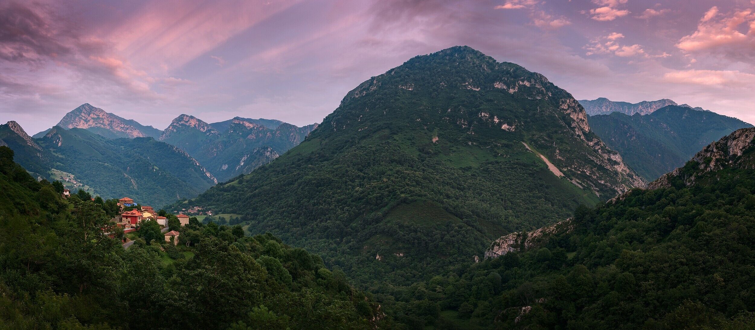 A mountainous landscape with a prominent peak, lush greenery, and a small settlement with buildings.