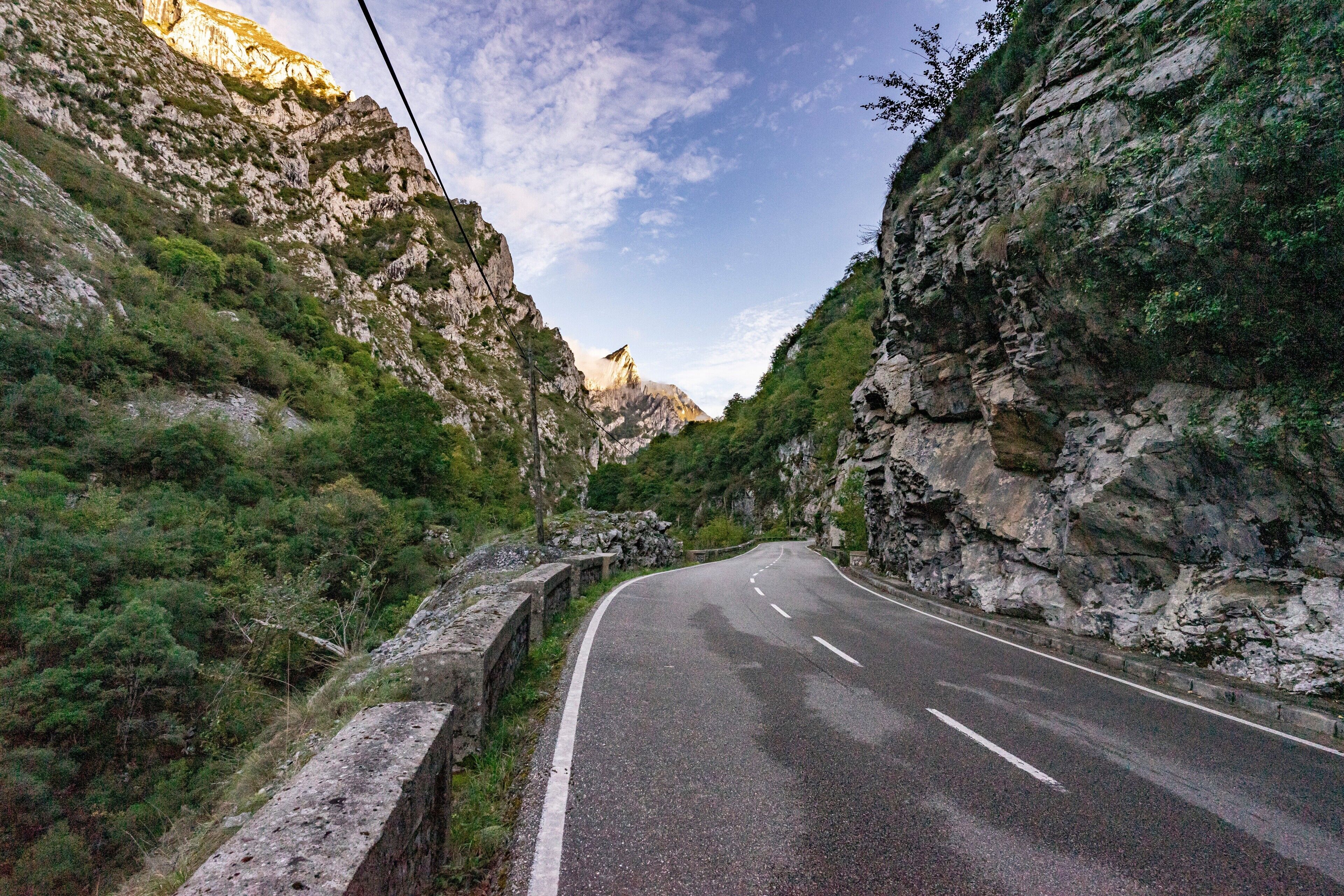 Een kronkelende bergweg, begrensd door rotsachtige kliffen en begroeiing.