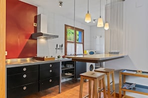 A modern kitchen with a red accent wall, a built-in oven, and a wooden island with stools. - Hot Tub with Mountain Views in Ponga Natural Park (Cazo)