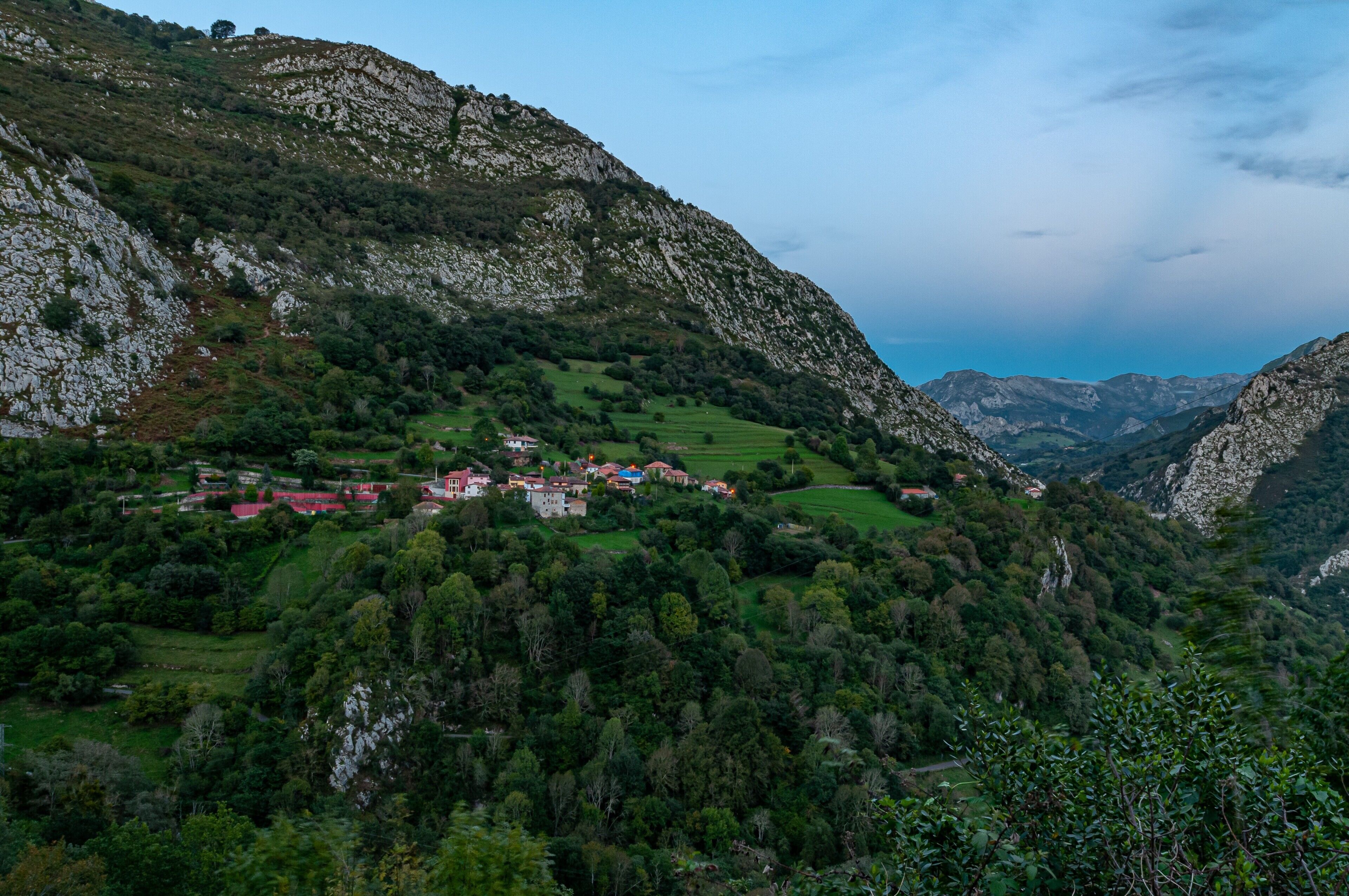 A mountainous landscape with a village nestled among green fields and rocky terrain.