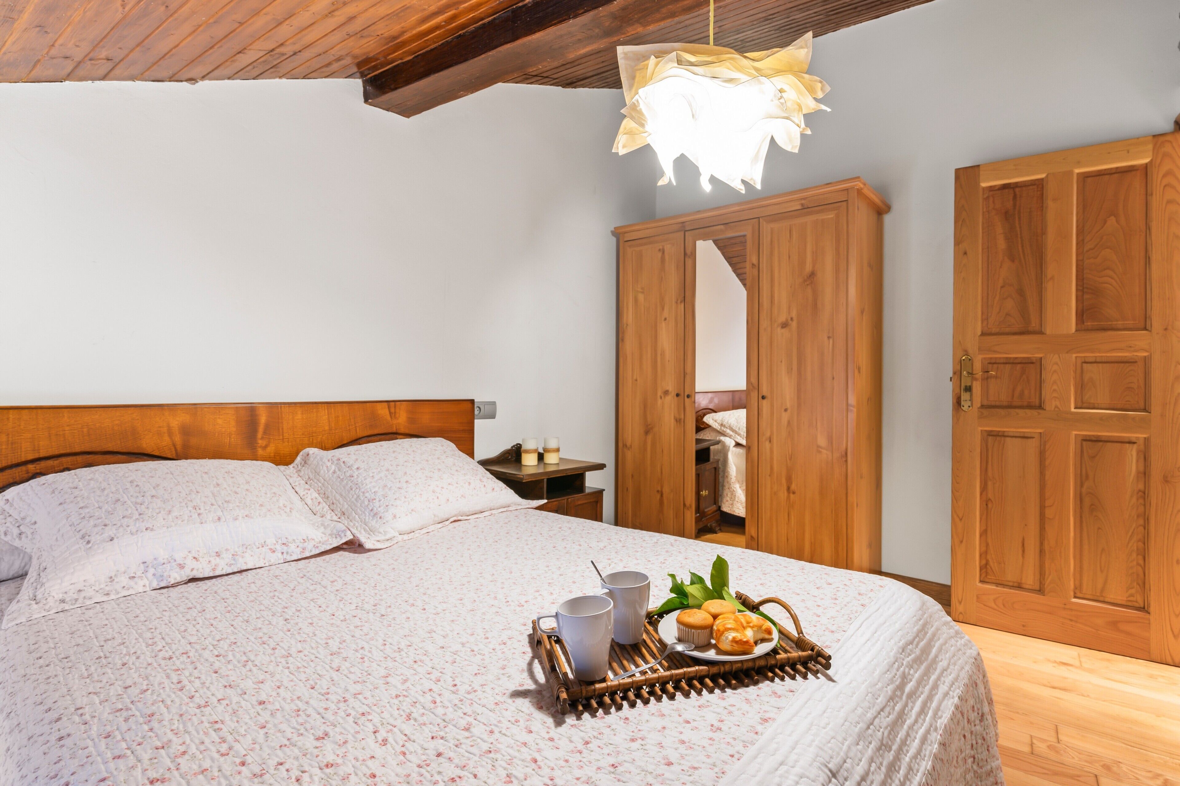 A bedroom with a wooden bed, a bedside table with candles, and a tray with pastries.