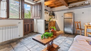 A kitchen with wooden beams, a refrigerator, a table with a basket of vegetables, and a window with a mountain view. - El Rincón del Sol: Retreat and Rest in the Picos de Europa. (Cazo)