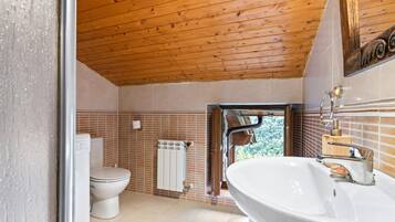 Un baño con techo de madera, inodoro y lavamanos blancos, y vistas a la vegetación exterior.