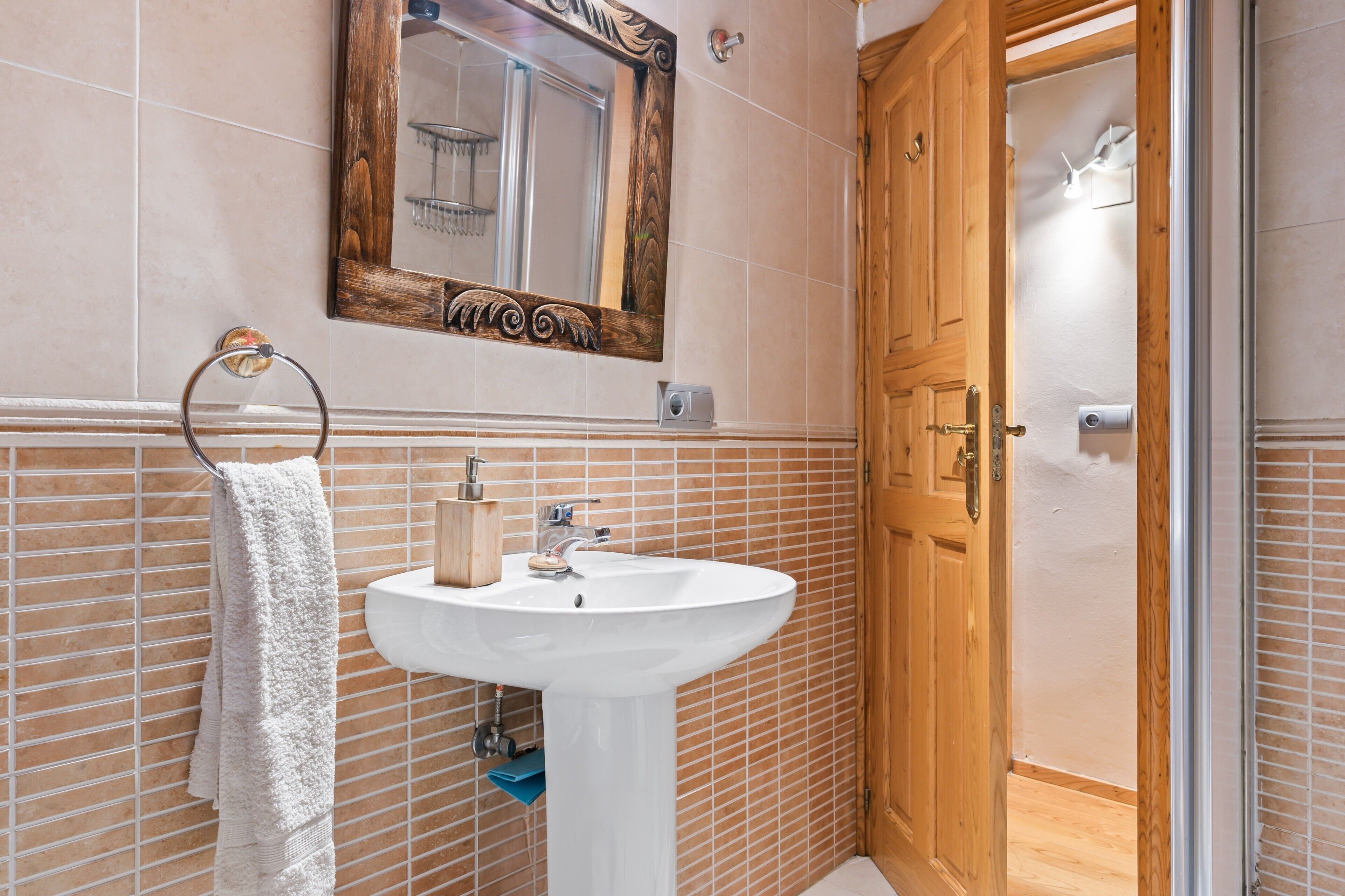 Ein Badezimmer mit einem weißen Waschbecken, einer Holztür und einem Spiegel mit dekorativem Rahmen.