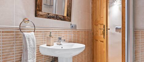 Ein Badezimmer mit einem weißen Waschbecken, einer Holztür und einem Spiegel mit dekorativem Rahmen.