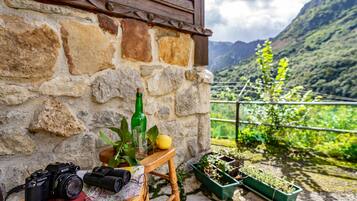 A stone wall, a wooden table with a camera, a bottle, a glass, and a lemon.