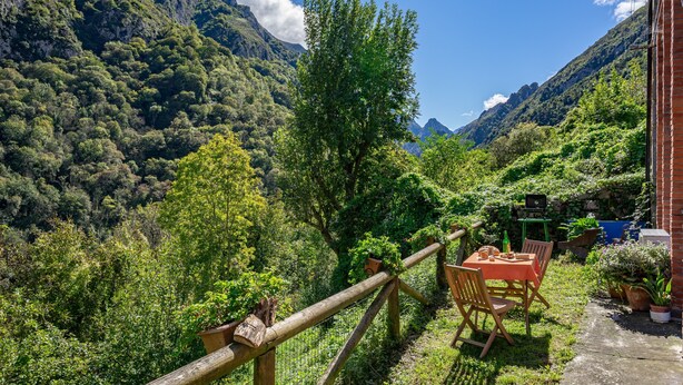 Een terras met een tafel en stoelen, omringd door weelderige begroeiing en bergen.