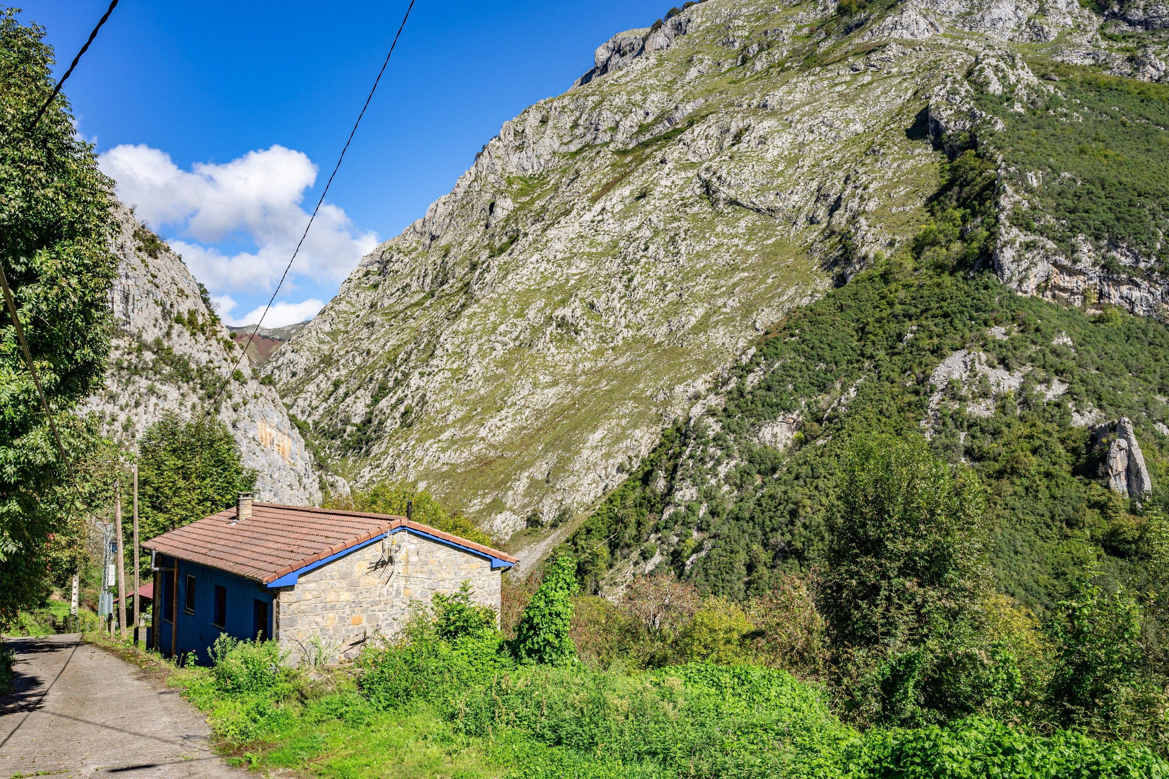 A stone building with a red roof, surrounded by lush greenery and rocky terrain.