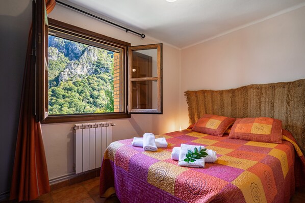 A bedroom with a large window, a bed with a colorful quilt, and a radiator.