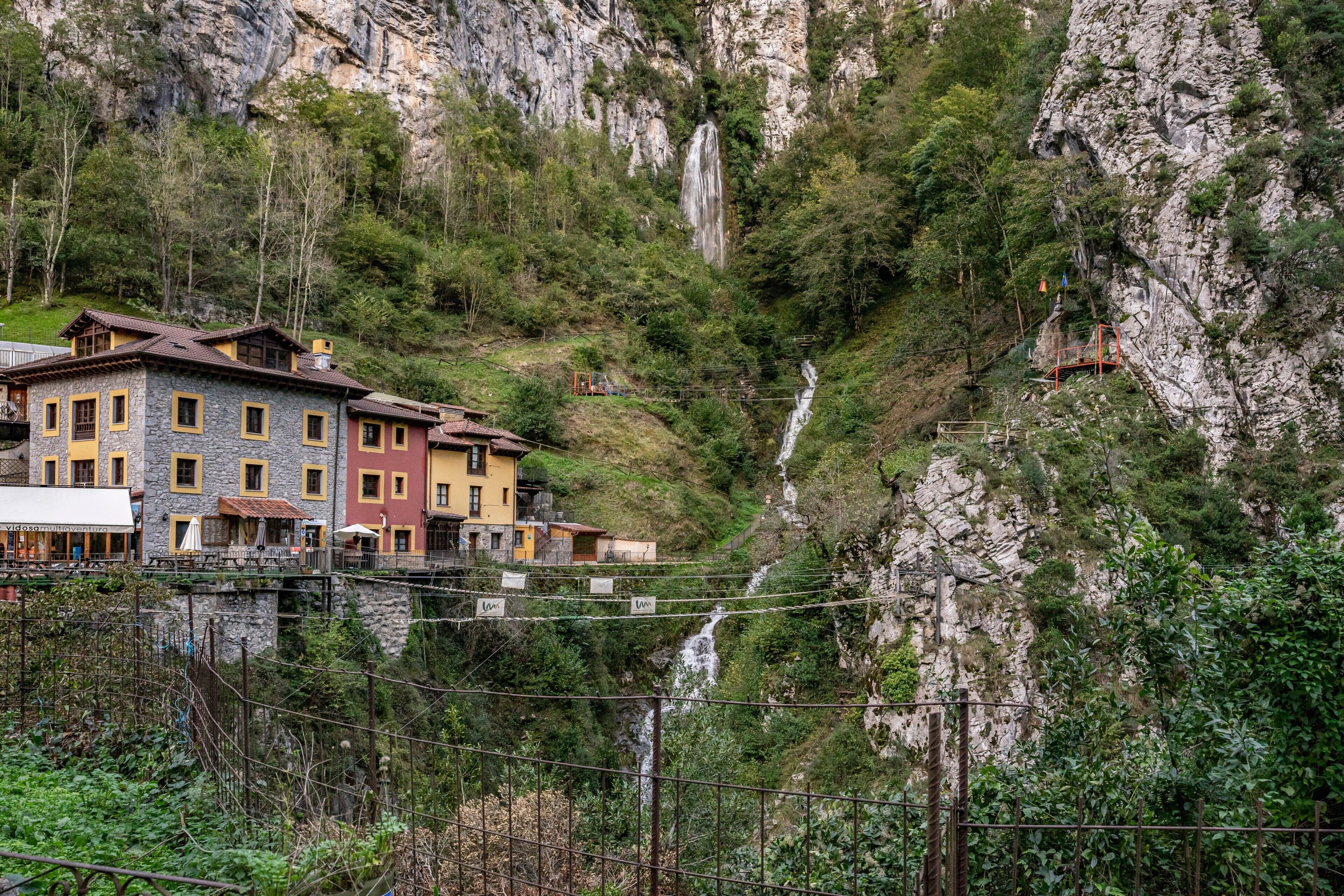 A mountainous area with a waterfall, buildings with balconies, and a bridge.