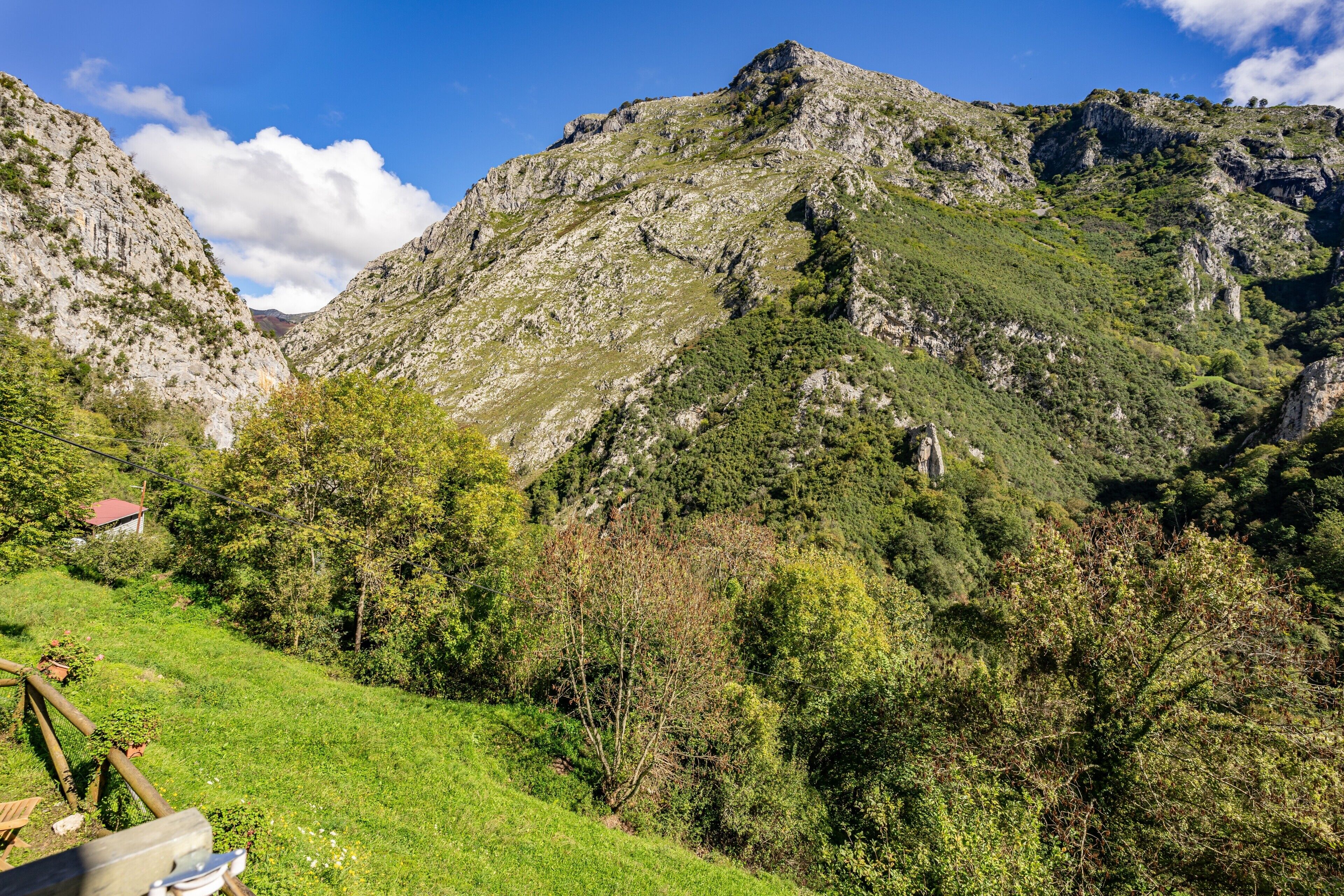 A mountainous landscape with a clear sky, a grassy area, and a small building.