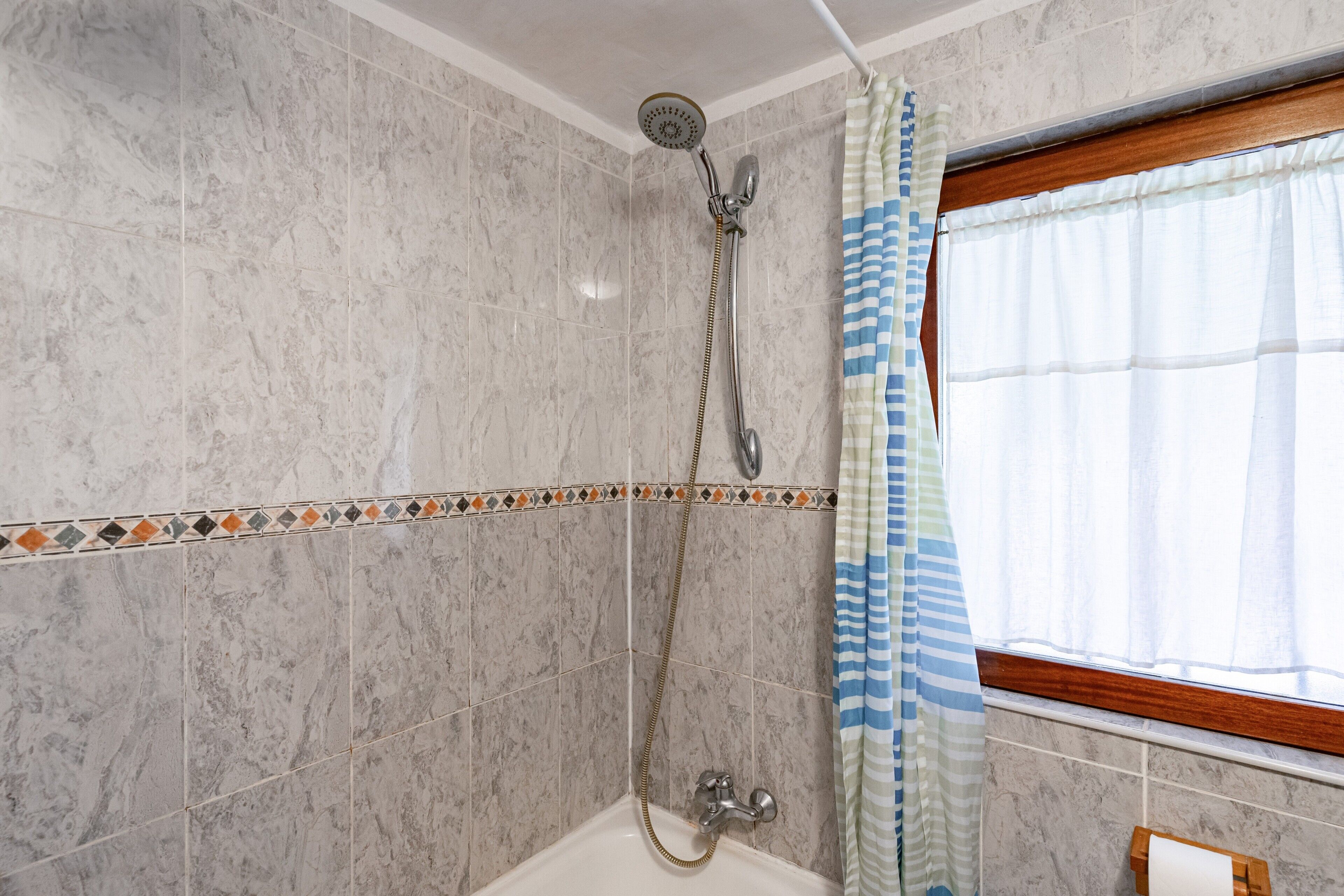 A bathroom with a shower, a window with a curtain, and a tiled wall.