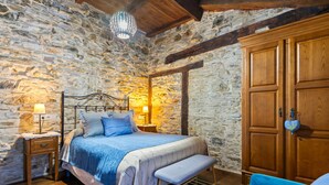 A bedroom with a stone wall, wooden bed frame, bench, and wardrobe. - Rural House 'Teixo' with Mountain Views, Private Terrace, and Wi-Fi (A Fonsagrada)