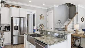 A modern kitchen with white cabinetry, a stainless steel refrigerator, granite countertops, and a wooden island with stools. - Park's Edge Home | Pool, Bike Trails, Beach Access | Three Seas Villa by Kaiser (Orange Beach)