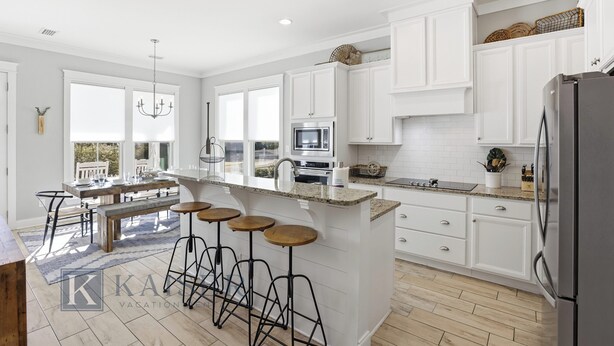 A modern kitchen with white cabinetry, a central island with stools, a built-in oven, and a refrigerator. - Park's Edge Home | Pool, Bike Trails, Beach Access | Three Seas Villa by Kaiser (Orange Beach)