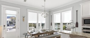 A modern kitchen with a wooden dining table, bench, and large windows.