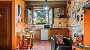 A kitchen with wooden cabinets, a dining table, a refrigerator, and a window with a view of greenery. - Casa Rural 'Nogueira' with Mountain Views, Private Terrace, and Wi-Fi (A Fonsagrada)