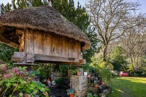 A rustic wooden structure with a thatched roof, surrounded by lush greenery and potted plants. - Rural House 'Loureiro' with Mountain Views, Shared Terrace, and Wi-Fi (A Fonsagrada)