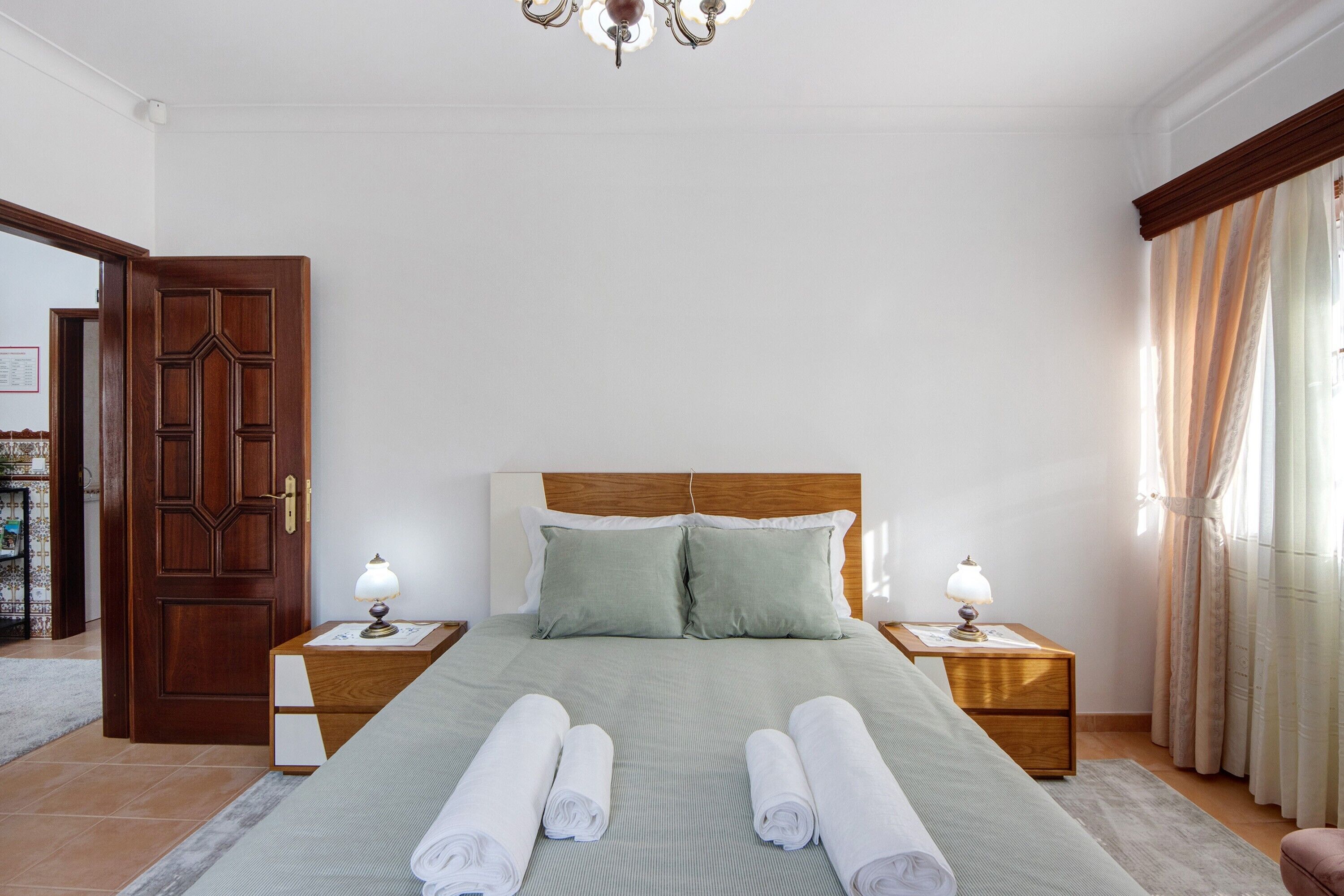 A neatly made bed with pillows, two bedside tables with lamps, and a wooden door.