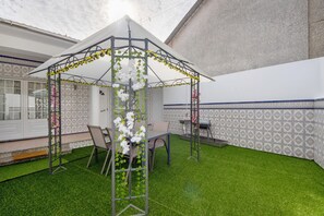 A gazebo with artificial grass, a table, chairs, and a patterned wall.