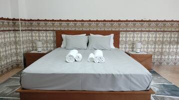Een net opgemaakt bed met kussens, een nachtkastje met een lamp, en een behangen muur.