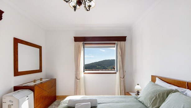 Une chambre d’hôtel équipée d’un lit, d’une commode, d’un miroir, d’un radiateur et d’une fenêtre donnant sur une colline.
