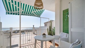 A balcony with a white table, chairs, a striped awning, and a view of the sea.