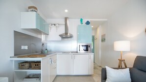 A compact kitchen with white cabinets, a stainless steel range hood, and a microwave.