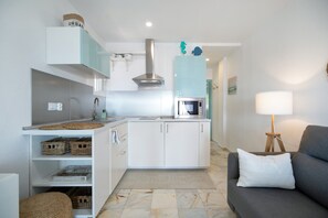 A compact kitchen with white cabinets, a stainless steel range hood, and a microwave.