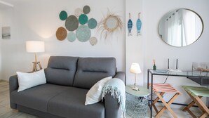 A modern living room with a grey sofa, a round mirror, a small table with a lamp, and a wall decorated with circular woven items.