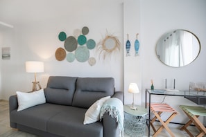 A modern living room with a grey sofa, a round mirror, a small table with a lamp, and a wall decorated with circular woven items.