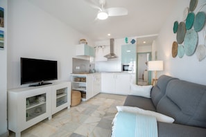 A modern living room with a flat-screen TV, a grey sofa, and a ceiling fan.