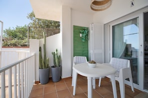 Un balcon avec une table et des chaises blanches, des cactus en pot et une porte verte.