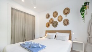 A hotel room with a large bed, a bedside table, a wall-mounted hat display, and a hanging plant.