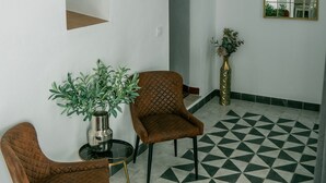 A room with a geometric patterned floor, two brown chairs, a round table with a plant, a white pendant light, and a mirror on the wall.