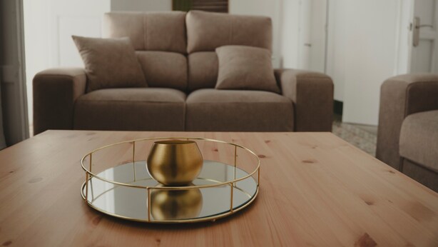 A round wooden table with a gold tray and a reflective bowl. In the background, there is a brown sofa and a white door.