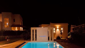 A swimming pool with a tiled deck, surrounded by a landscaped garden and a modern house with illuminated windows. - Pazuri at Vipingo  (Kibaoni)