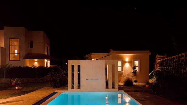 A swimming pool with a tiled deck, surrounded by a landscaped garden and a modern house with illuminated windows. - Pazuri at Vipingo  (Kibaoni)