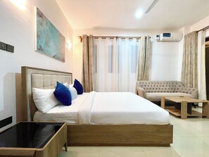 A hotel room with a bed, a sofa, a small table, and an air conditioning unit.