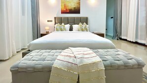 A modern bedroom with a large bed, a headboard, a bedside table with a lamp, and a wall-mounted artwork. - Pazuri at Vipingo  (Kibaoni)