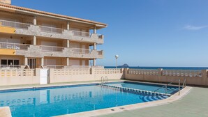 Una piscina con vista despejada al océano y un edificio de varios pisos con balcones.