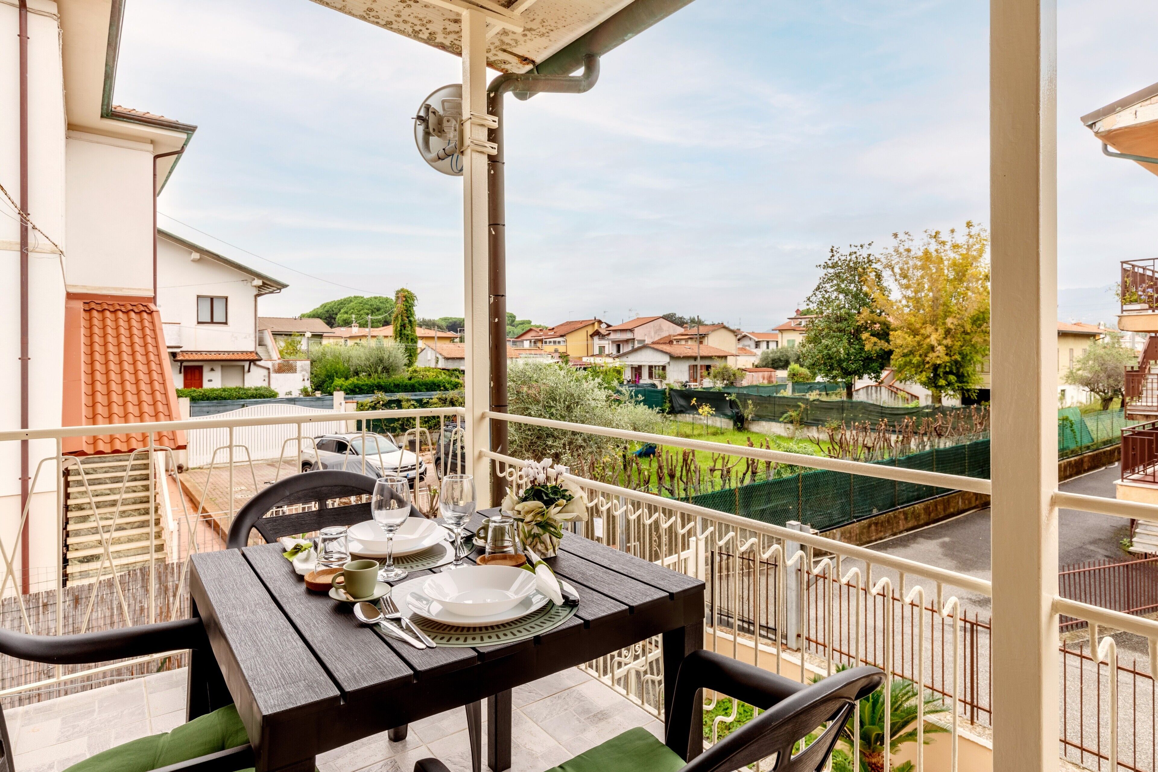 A balcony with a table set for dining, chairs, and a view of a residential area.